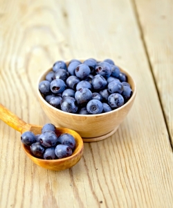 Blueberries in wooden bowl and spoon on board